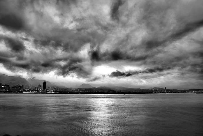 Black and white seascape with cloudy sky over city skyline