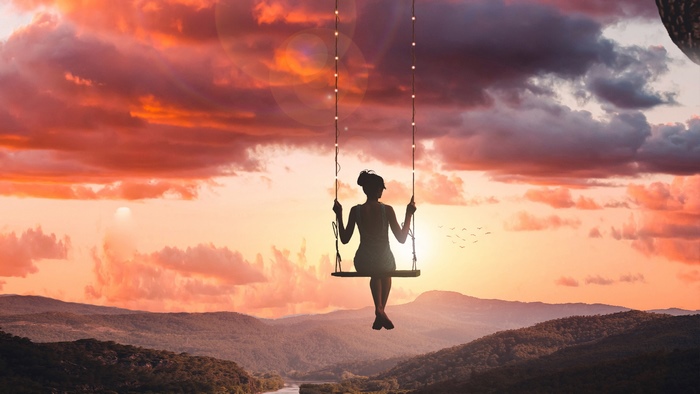 Silhouette of a girl on a swing at sunset