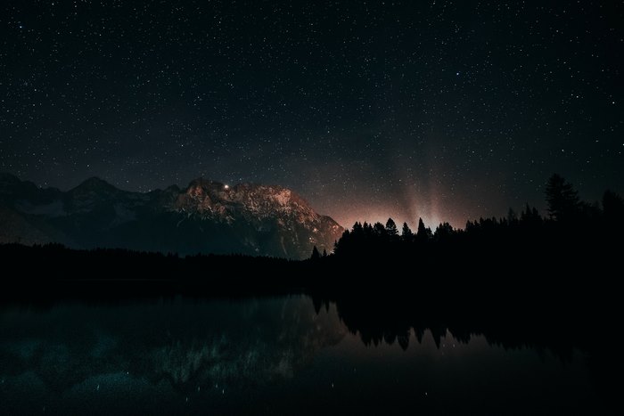 Mountain lake under starry night sky with reflection