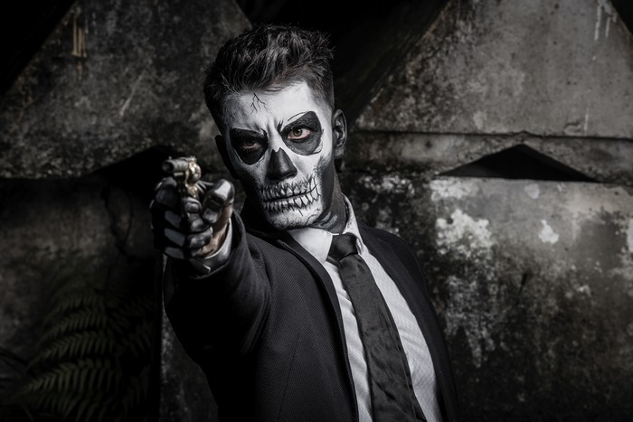 Man with skull face paint holding a gun
