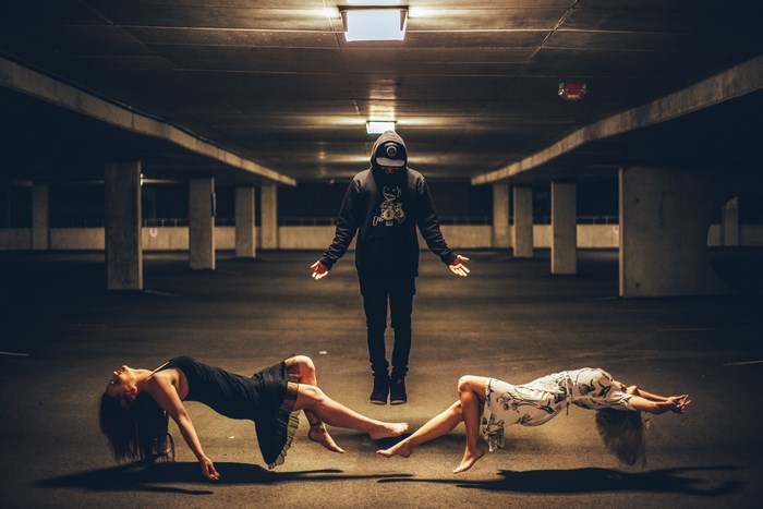 Man in hoodie levitating two women in parking garage