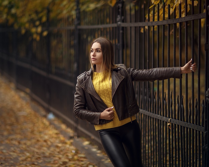Woman in leather jacket leaning on a fence