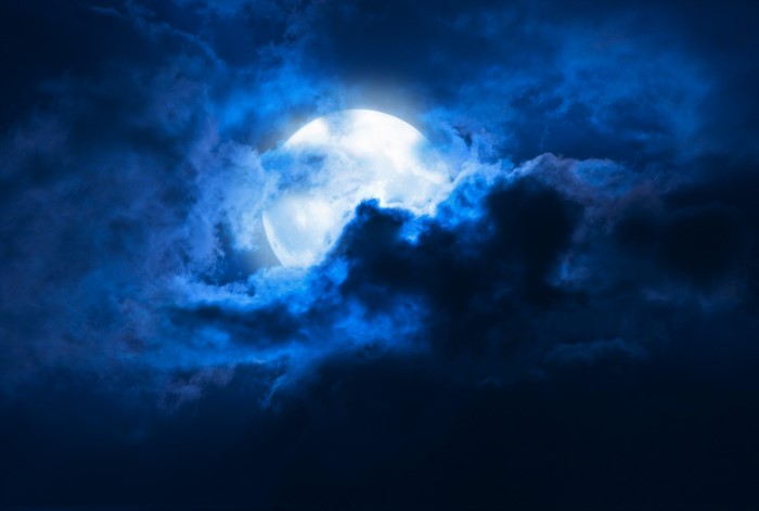 Full moon behind dark blue clouds at night