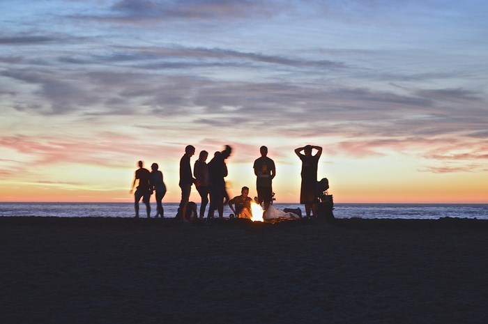 People silhouetted around a bonfire at sunset on a beach
