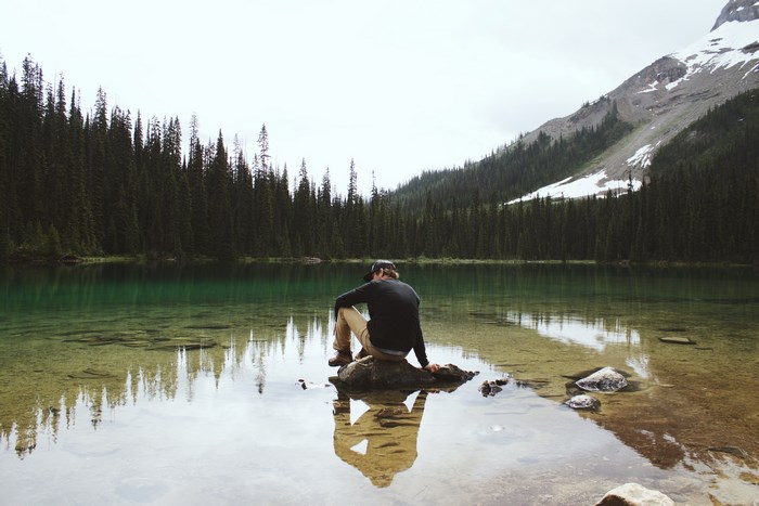Man sitting on rock in lake with forest and mountain background