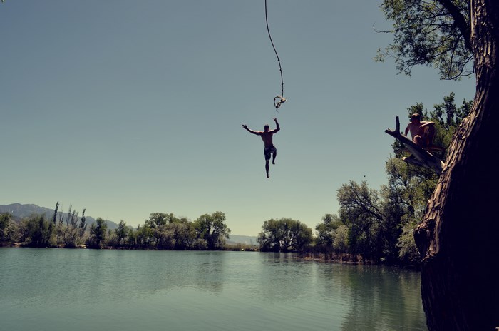 Man jumping with rope swing over lake