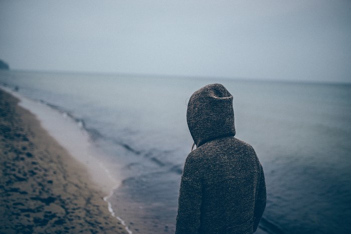 Person in hoodie looking out at the sea from a beach