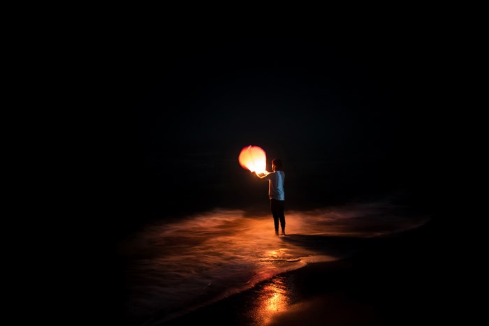 Person holding a glowing sky lantern on a beach at night