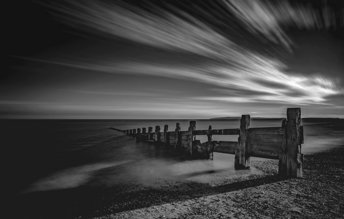 Long exposure of wooden sea defense with streaking clouds
