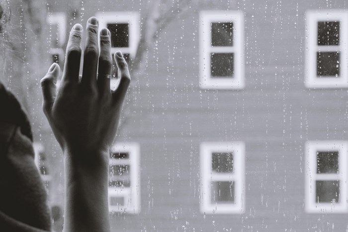 Hand on a rainy window looking at building