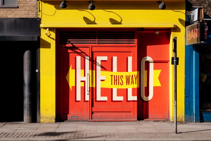 Red door with "Hello This Way" text and yellow arrow