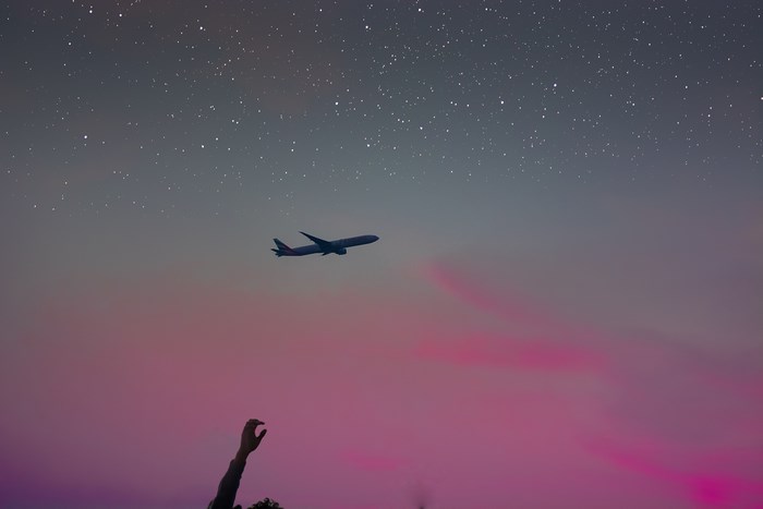 Airplane flying in a starry pink sky with a reaching arm