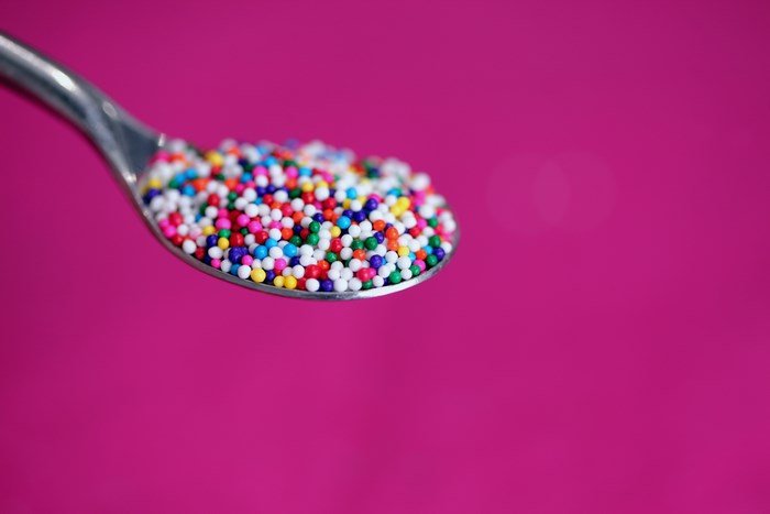 Spoonful of colorful sprinkles on a pink background