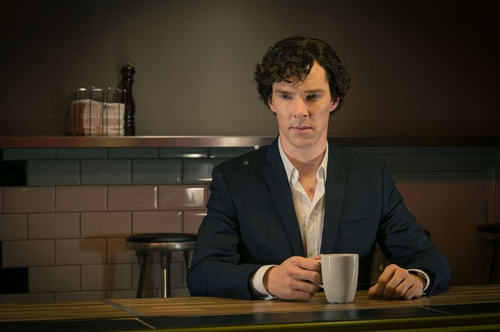 Sherlock Holmes sitting with a mug