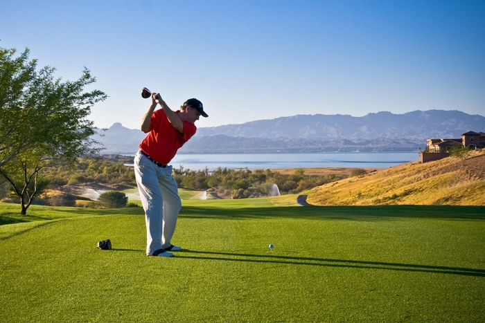 Golfer swings club on a sunny golf course with lake and mountains