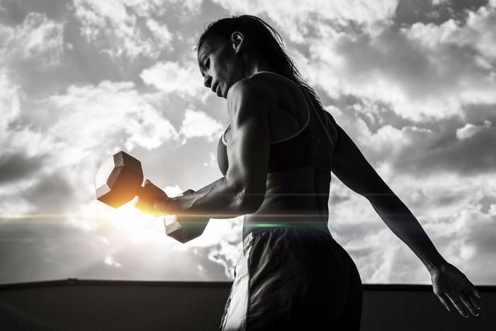Woman lifting dumbbell against cloudy sky
