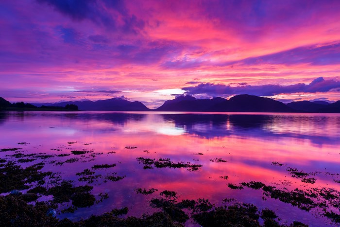 Purple and pink sunset over a calm lake with mountains