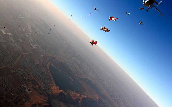 Wingsuit divers jump from a helicopter over a city