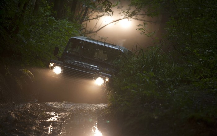 Land Rover Defender driving through a muddy forest