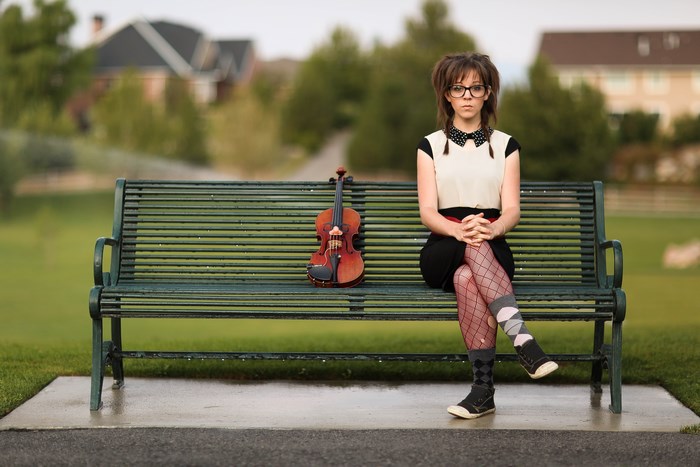 Lindsey Stirling sitting on a park bench with a violin