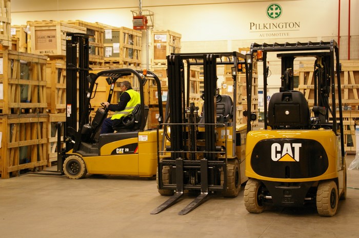Forklifts in a warehouse with Pilkington Automotive logo