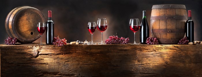 Wine bottles, glasses, grapes, and barrels on a wooden table