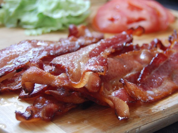 Crispy bacon strips on a wooden cutting board with lettuce and tomato