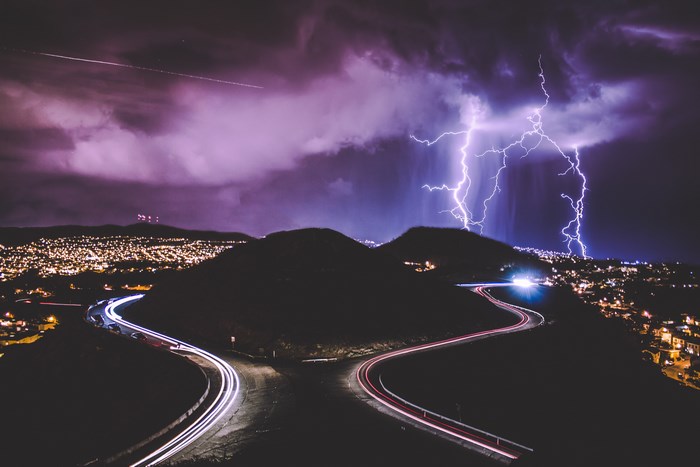 Lightning strikes over a city at night with light trails on roads