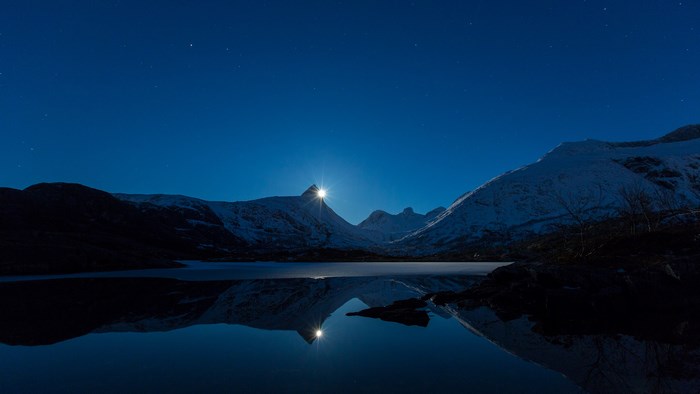 Moonlight over snow-capped mountains and lake