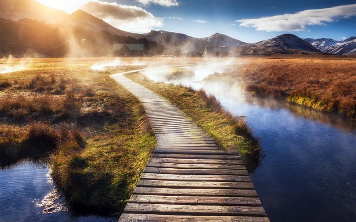 Wooden boardwalk through misty landscape with mountains