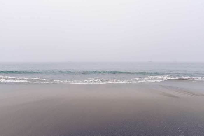 Foggy beach with ocean waves and distant ships