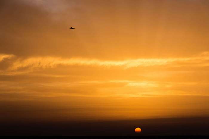 Airplane flying in orange sunset sky with clouds