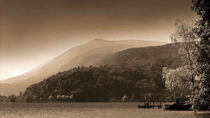 Sepia landscape of misty mountains over a lake with a dock
