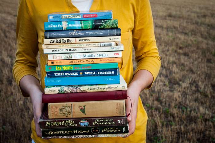 Stack of Books Held by Person in Yellow Shirt