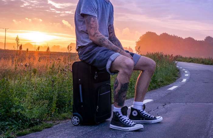 Man with tattoos sitting on suitcase at sunset