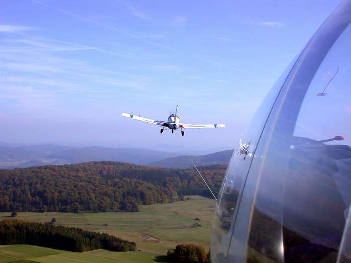 Glider being towed by a plane over rolling hills