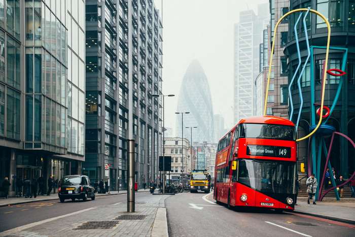 Red double-decker bus on a city street with skyscrapers