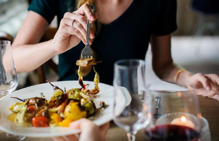 Woman eating roasted vegetables with a fork at a table