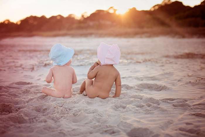 Two babies in bonnets on a beach at sunset