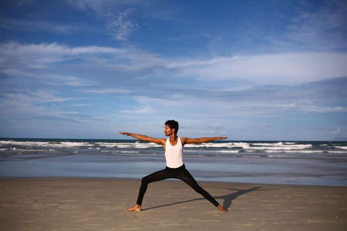 Woman practicing yoga warrior pose on beach