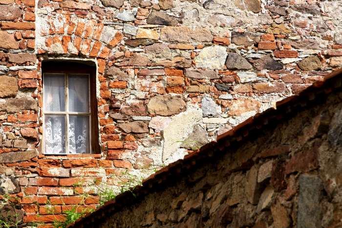 Old brick wall with a window and a tiled roof