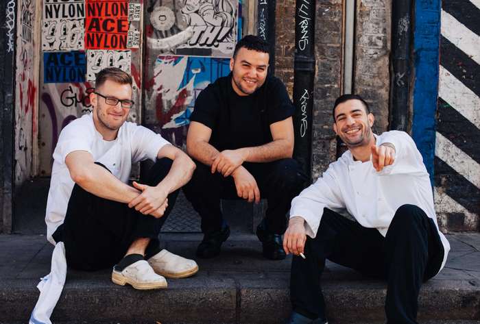Three men in chef attire posing on a city street