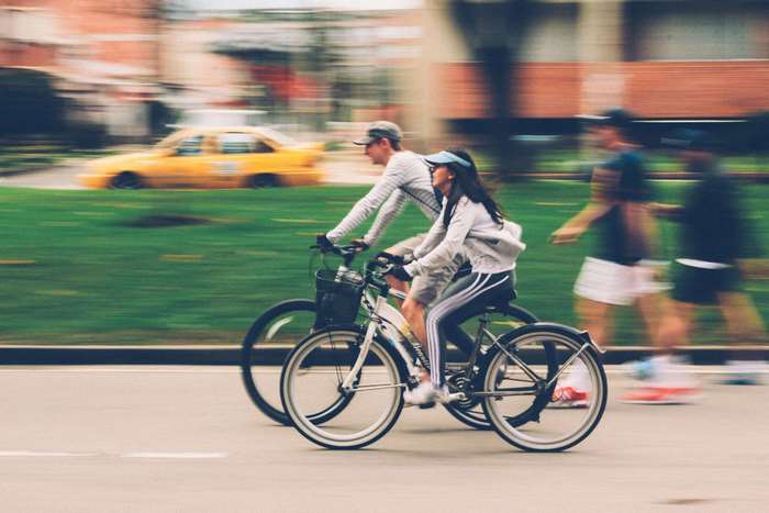 Couple cycling on a street with a yellow taxi