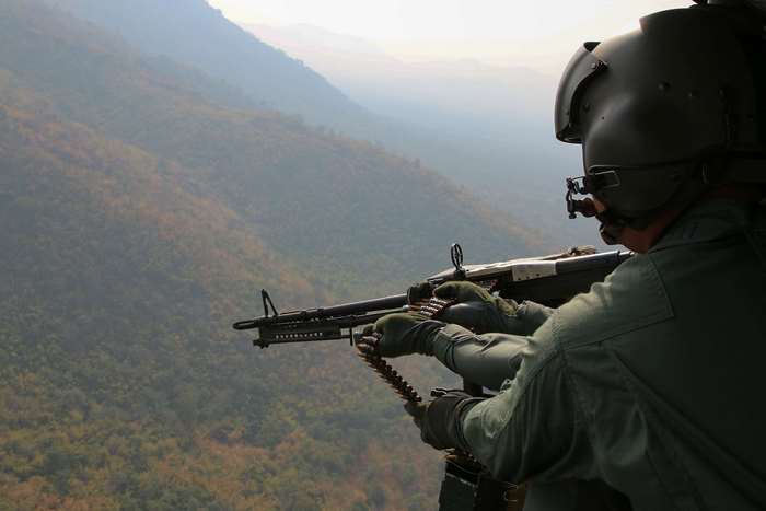 Man with machine gun in helicopter overlooking mountains