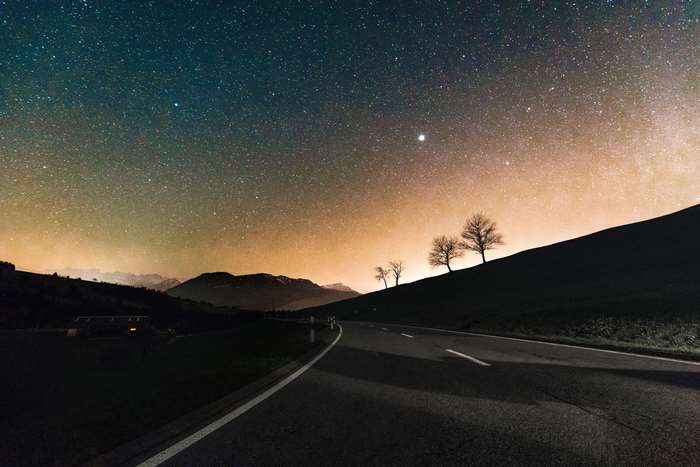 Road under starry sky with trees and mountains