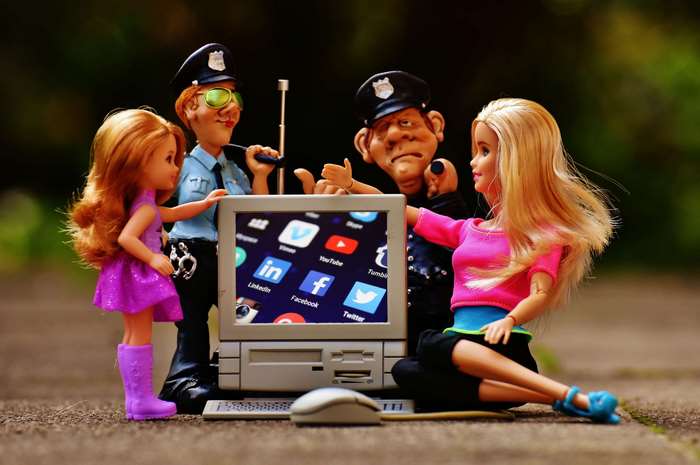 Dolls and police figures interact with a computer displaying social media icons