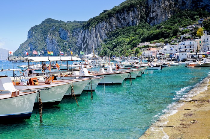 Boats docked in a harbor with a cliffside town in Capri, Italy