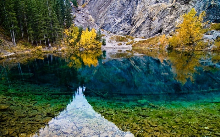 Turquoise lake reflecting autumn trees and rocky mountains