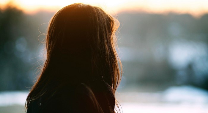 Girl with long brown hair looking out at sunset