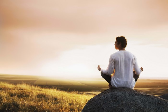 Man meditating on a rock at sunrise